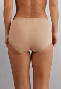 Beige katoenen slip met golvende kantafwerking op de tailleband. Zachte textuur, volledig dekkend ontwerp en naadloze randen voor comfort.
