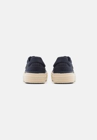 Navy canvas slip-on shoes with a textured beige espadrille sole. Back view shows padded collar and stitching details.