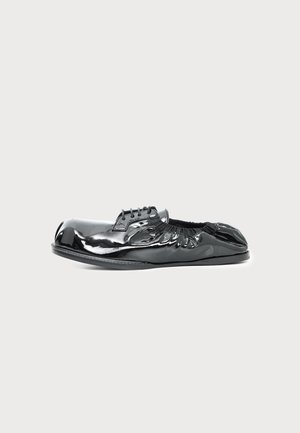 Une chaussure plate en cuir verni noir brillant, à lacets et à ouverture élastique froncée, sur un fond clair uni.