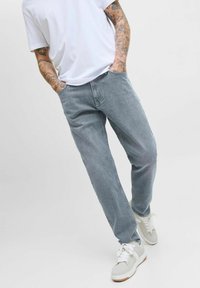 Vaqueros de mezclilla gris claro con un corte recto, que cuentan con bolsillos frontales y un diseño simple y minimalista, combinados con zapatillas blancas.