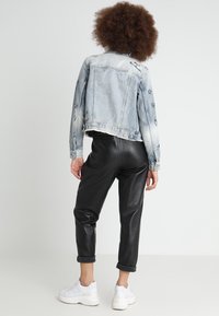 Jeansjacka med ljusblå tvätt, broderade detaljer, ihopparad med svarta läderbyxor och vita sneakers. Bakifrån, kort design.