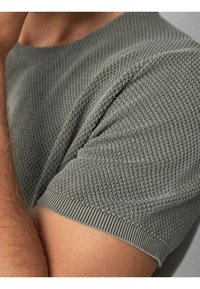 Maglietta a maniche corte verde oliva in maglia con un motivo texture e rifiniture a costine sul colletto e sulle maniche, che mette in risalto un design aderente.