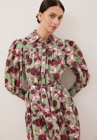 Kwiatowa sukienka na jasnoszarym tle, z głębokimi czerwonymi i różowymi różami, zapinana na guziki z przodu, z bufkami i paskiem w talii.