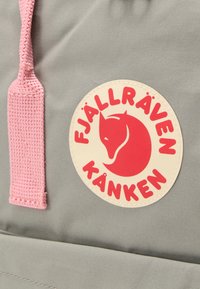 Ανοιχτό γκρι σακίδιο με υφασμένους ροζ ιμάντες, που διαθέτει έναν κυκλικό μπεζ λογότυπο με τη μορφή κόκκινου αλεπού και το κείμενο "FJÄLLRÄVEN KÅNKEN".