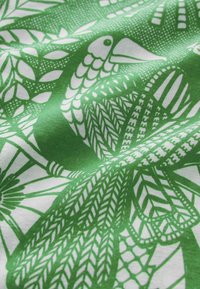Tissu vert et blanc avec une illustration détaillée d'un oiseau présentant des ailes à motifs et des motifs de feuilles autour.