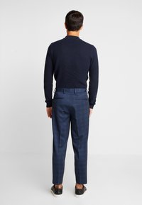 Navy textured sweater with ribbed detail paired with tailored patterned trousers, featuring side pockets and dark footwear.