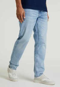 Hellblaue Jeans im entspannten Schnitt mit subtilen Ausbleichungen und kontrastierenden Nähten, kombiniert mit weißen Sneakers.