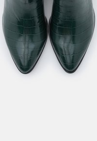 Tmavě zelené kotníkové boty s embosovaným krokodýlím vzorem, s špičatou špičkou a hladkým povrchem, s elegantním designem a stylovou siluetou.