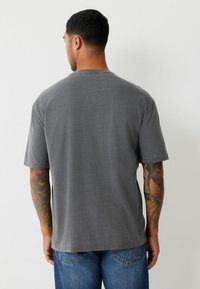 Szürke pamut rövid ujjú póló kerek nyakkivágással és laza szabással. Egyszínű, mintázat nélküli dizájn, kék farmernadrággal párosítva.