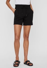 Shorts noirs avec une ceinture élastique froncée, des détails à cordon, des poches latérales et une coupe décontractée, associés à des sandales noires.