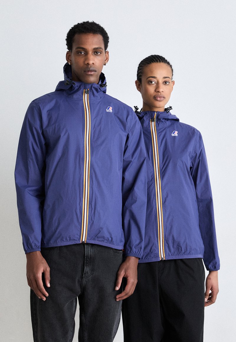 Blue lightweight jackets with a zip front, featuring multicolored stripes, adjustable hoods, and elastic cuffs. Two models wear them.