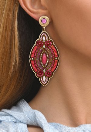 De grandes boucles d'oreilles ornées avec une base en ton doré, des pierres roses et rouges dans un design floral et symétrique, suspendues à un attachement à clou.