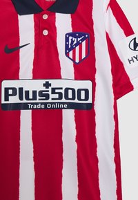 Camiseta de fútbol a rayas rojas y blancas con cuello negro, logo de Nike, escudo del equipo y un logo de patrocinador en texto negro en negrita.