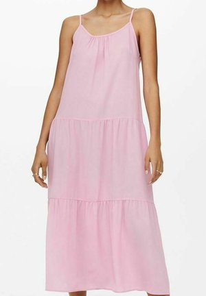 Mujer con vestido midi sin mangas, rosa claro, de capas y con tirantes finos, sobre un fondo blanco liso.