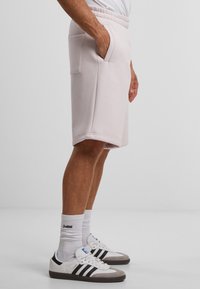Lys rosa bomullsshorts med snøring i livet og sidelommer, sammen med hvite og grå sneakers og hvite sokker.