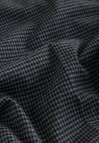 Tessuto tessile con un motivo a quadri grigio scuro e nero, texture morbida, con pieghe e drappeggi visibili.