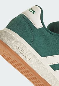 Gröna mockasneakers med vita accenter, texturerad gummisula och tre ränder design. Logotypen är placerad på baksidan.