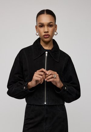 Zwarte suède cropped jack met een grote kraag, ritssluiting aan de voorkant en details van zilver hardware. Geconfigureerde stof en een losse pasvorm.