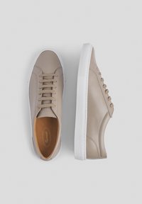 Zapatillas de cuero beige con una textura suave, que cuentan con un cierre de cordones en la parte delantera, suela de goma blanca y sutileza en los detalles de costura en los costados.