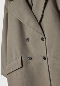 Manteau en laine taupe à double boutonnage avec de larges revers, quatre boutons noirs et des poches à rabat de chaque côté.