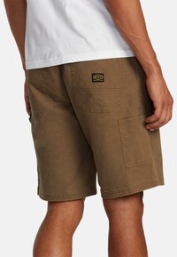 Brune cargoshorts lavet af et robust materiale, med sidelommer og et synligt varemærke på bagsiden. Kort indersøm og afslappet pasform.