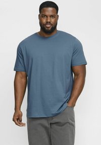 Camiseta de algodón azul con cuello redondo y mangas cortas, con un corte relajado y una textura suave. Combinada con pantalones cortos gris claro.