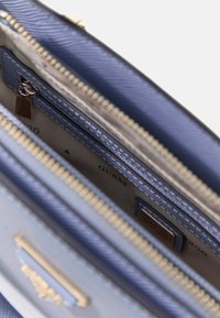 Lichtblauwe gestructureerde handtas met gouden accenten, ritsvakken en een gestructureerd oppervlak. Binnenkant heeft een logodetail.