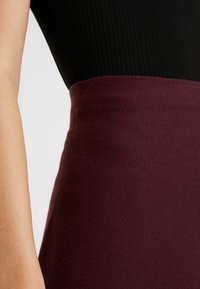 Zwarte geribbelde top gaat over in een effen bordeauxrode trui onder de taille, met een gladde textuur en een aansluitend ontwerp.