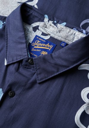Granatowa koszula z guzikami z kwiatowym wzorem w jasnoniebieskim i białym kolorze. Wykonana z tkaniny o gładkiej fakturze. Zawiera metkę od Superdry.