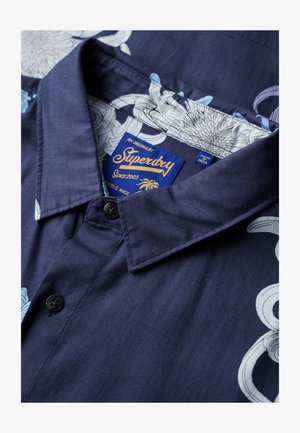 Granatowa koszula z guzikami z kwiatowym wzorem w jasnoniebieskim i białym kolorze. Wykonana z tkaniny o gładkiej fakturze. Zawiera metkę od Superdry.