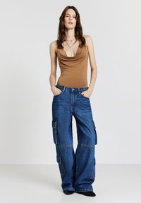 Body con con collo a dolce in marrone abbinato a jeans cargo a gamba larga blu caratterizzati da tasche laterali e una vestibilità rilassata. Tessuto morbido con un aspetto informale.