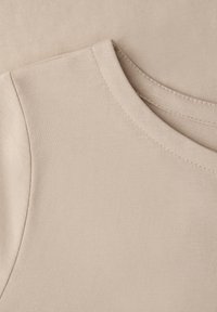 Gros plan sur un tissu de T-shirt en coton beige montrant l'encolure et les coutures d'épaule avec des détails de couture fins.