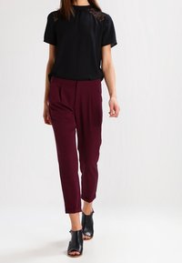 Blusa negra de manga corta con detalles de encaje, combinada con pantalones ajustados burdeos. Zapatos de tacón abiertos negros completan el conjunto.