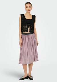 Gilet nero in crochet con design a rete, legato davanti, abbinato a una gonna midi plissettata lavanda e ballerine nere.