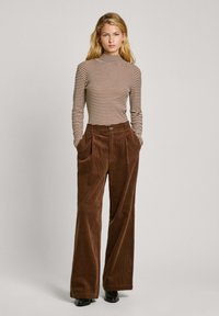 Top de cuello alto a rayas en beige y marrón, combinado con pantalones de pana marrones de pierna ancha que presentan bolsillos frontales y una sutil textura.