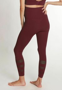 Les leggings taille haute bordeaux présentent des panneaux en mesh sur les jambes inférieures ; fabriqués en tissu extensible pour le confort et la liberté de mouvement.