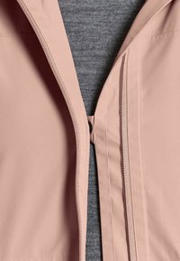 Nahaufnahme einer teilweise geöffneten hellrosa Jacke über einem grauen, gerippten Pullover, die Nähte und Reißverschlussdetails zeigt.