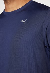 Náměsíčná modrá košile s krátkým rukávem a žebrovanou strukturou, kulatým výstřihem. Obsahuje malé stříbrné logo Puma na hrudi.