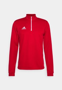 Punainen pitkähihaista urheilupuseroa, jossa on valkoinen neljänneksen vetoketju ja valkoinen Adidas-logo vasemmassa rinnassa.
