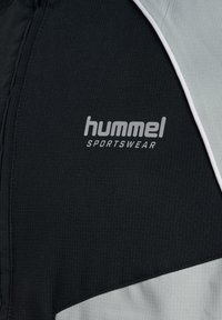 Mustvalge ja hall Hummel spordiriietus, millel on tekstuuriga kangas, esiküljel on selgelt nähtav valge aktsent ja logo.