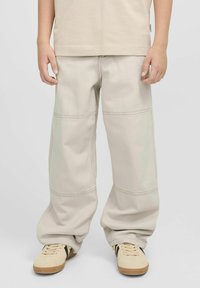 Beige laiad jalatsid nähtavate õmblustega, millel on kombineeritud heledad tenniseketsid. Kanga tekstuur on pehme ja sile.