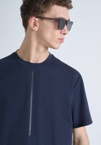 T-shirt blu navy a maniche corte con un sottile dettagli verticale a righe nere sul davanti; realizzato in tessuto liscio con scollo rotondo.
