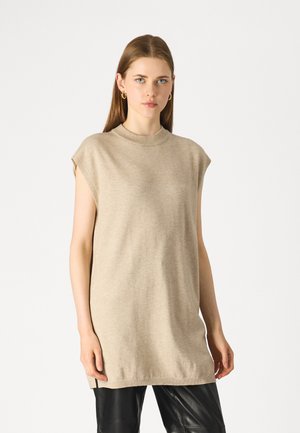 Beige knit sleeveless tunic with a high neck, featuring a smooth texture and side slits, paired with black leather pants.