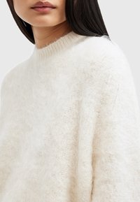 Leichter, cremefarbener Pullover aus flauschigem Material mit hohem Kragen und gerippten Details, der eine lockere Passform und eine weiche Textur bietet.