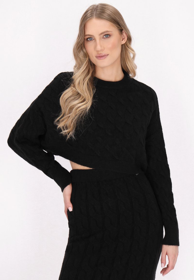 Schwarzer, kabelgestrickter, kurz geschnittener Pullover mit langen Ärmeln, kombiniert mit einem passenden schwarzen, kabelgestrickten Rock, der ein strukturiertes Muster und einen elastischen Taillenbund aufweist.