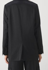 Czarna dopasowana marynarka z teksturowanego materiału, z długimi rękawami i pojedynczym rozcięciem z tyłu. Posiada guziki na mankietach oraz usztywniany kołnierz.