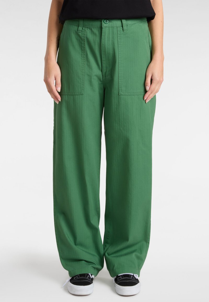 Groene cargobroek met wijde pijpen, gemaakt van zachte stof, met twee grote voorzakken en een gladde textuur. Draagt met zwarte sneakers.