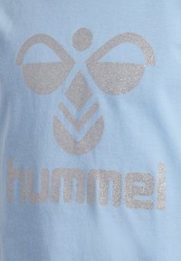 Himmelblaues T-Shirt mit einem silbernen Glitzer-Logodesign, das eine stilisierte Biene und den Markennamen "hummel" in Großbuchstaben zeigt.