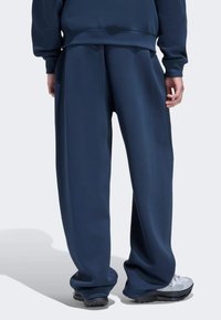 Tummansinisiä collegehousuja, löysä istuvuus, sileä pinta, joustava vyötärönauha, yhdistettynä valkoisiin urheilukenkiin, minimalistinen muotoilu.