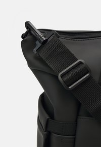 Czarna torba o gładkiej fakturze, z zamknięciem na zamek błyskawiczny i nylonowym paskiem z metalowym klipsem. Zawiera szybkozłączkę.